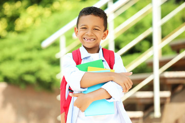 Young African American school boy with backpack and books on the street
