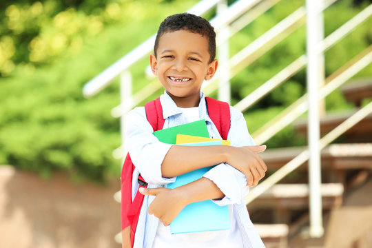 Young African American school boy with backpack and books on the street