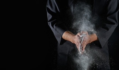 Fototapeta na wymiar Male hands and splash of white wheat flour on a black background