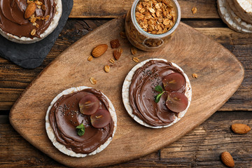 Puffed rice cakes with chocolate spread and grape on wooden table, flat lay