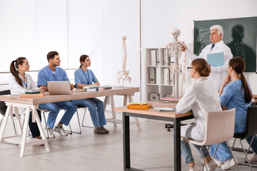 Medical students and professor studying human skeleton anatomy in classroom