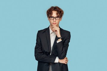 Freestyle. Young businessman in suit and glasses standing isolated on gray looking camera cunning