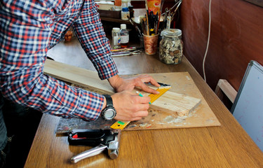 A man works in a joiner's shop, working with a tree. Man draws marks on wood with a ruler. 