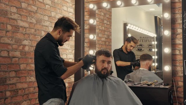 Hairdresser doing hair cut with hair machine for brutal man in barber shop. Barber making hairstyle with electrical shaver in male salon. Bearded man in barber shop