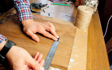 A man works in a joiner's shop, working with a tree. Man draws marks on wood with a ruler.