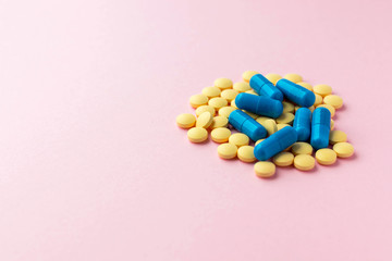Heap of round yellow pills and blue capsules on light pink background. Prescription drugs. Woman health. Epidemic, painkillers, healthcare and treatment concept. Copy space.