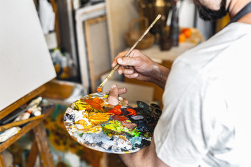 Male painter at art studio indoors mixing colors on palette back view close-up