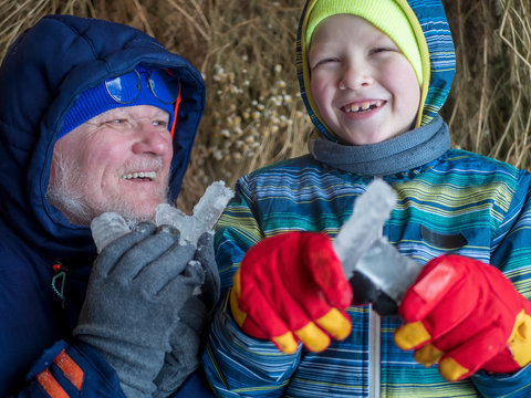 elderly man father and one child in winter clothes and bright gloves holding icicles in their hands. Bunches of dry grass hang in barn. Family happy together on winter vacation
