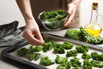 Poster Woman preparing kale chips at table, closeup © New Africa