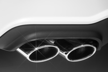 Double chrome exhaust pipe of sport car with white bodywork and plastic bumper, automobile industry, selective focus, monochrome shot