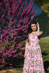 Beautiful woman stand by violet blooming tree. Blue background. Fashion model