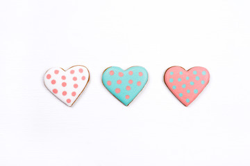 Three gingerbread cookies with frosting in the shape of a heart on white wooden background. Valentines day concept. Flat lay, top view.