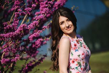 Beautiful woman stand by violet blooming tree. Blue background. Fashion model