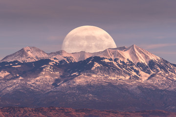 Full moon at it's perigee rising behind La Sal Mountains in Canyonlands National Park during sunset - obrazy, fototapety, plakaty