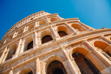 Obraz premium Colosseum or Coliseum ancient ruins background blue sky Rome, Italy, view from below, stone arches and sunrays