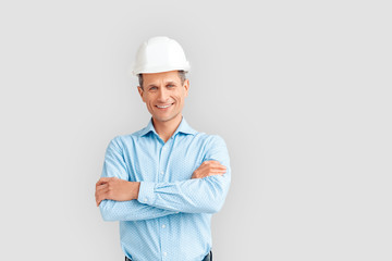 Construction. Mature man in hardhat standing isolated on white crossed arms smiling playful