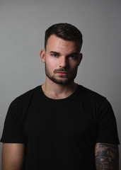  Portrait of young and fit fashion model with tattoos on grey background. Portrait of pretty young guy with short hair - rembrandt lighting. Shot of man with grey tones