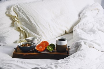 Hygge healthy breakfast in bed. Food tray with coffee and fruits on the white bed linen background