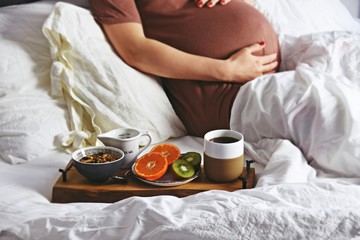 Obraz na płótnie Canvas Pregnant woman is having a healthy breakfast in bed. Pregnant woman in a bed on white linen background