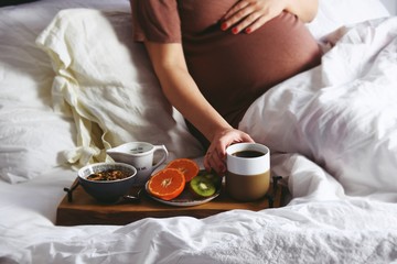 Fototapeta na wymiar Pregnant woman is having a healthy breakfast in bed. Pregnant woman in a bed on white linen background