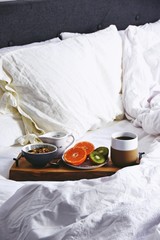 Hygge healthy breakfast in bed. Food tray with coffee and fruits on the white bed linen background
