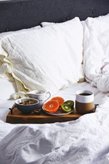 Obraz na płótnie Canvas Hygge healthy breakfast in bed. Food tray with coffee and fruits on the white bed linen background