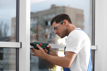 Construction worker repairing plastic window with electric screwdriver indoors