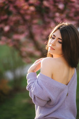Fototapeta premium Attractive young woman in a purple sweater stand in front of sakura tree in the park