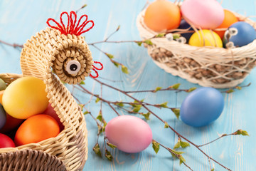 Wicker basket in the form of a chicken with colorful Easter eggs on blue table - easter composition