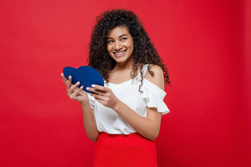 Naklejka premium playful black girl flirting with blue heart shaped valentine card isolated over red