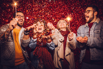 Group of happy friends celebrating New Year with sparklers and confetti. New year party.