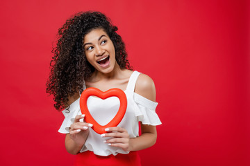 happy smiling black woman with heart shape looking at copyspace isolated over red