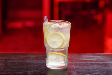 Closeup of a refreshing lemon Gin Spritz Cocktail, standing on the bar counter, isolated on a red light background.