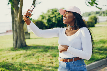 Stylish girl in a summer park. Woman in a blue jeans and pink cap. Famale with smartphone