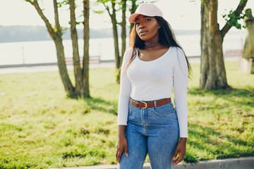 Stylish girl in a summer park. Woman in a blue jeans and pink cap