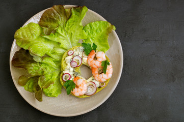 green bagel with cheese and shrimp. on a gray background.