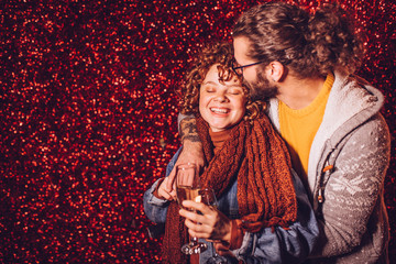 Young couple drinking champagne in front of the red glitter wall. New year party