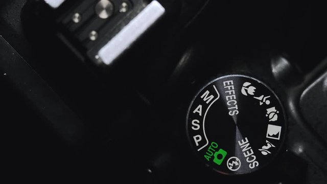 Close-up hands of a male photographer are switching mode on modern digital camera. turn the tuning wheel to manual mode.