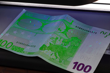 100 Euro banknote. Lying in the ultraviolet to verify the authenticity of banknotes. Close-up