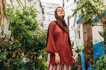 Muslim woman on the street of the blue city of Morocco stands at the bushes of greenery, lifting...