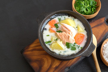 Salmon soup with cream, potatoes, carrots and dill. on a black background.