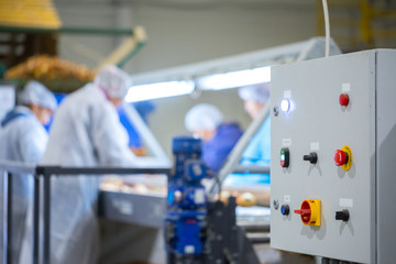 Device control panel of conveyor sorting line. Production facilities for grading, packing and storage of crops, foods or goods of large agricultural companies. Workers in defocus in the background.