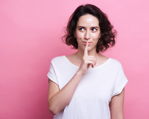 Good looking young Caucasian woman in round transparent eyewear, keeps hand raised, dressed in casual outfit, pretends holding something wonderful, isolated over pink background. Look there