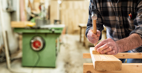 Close-up. Carpenter with hammer and nails fixes a wooden board. Construction industry, do it yourself. 