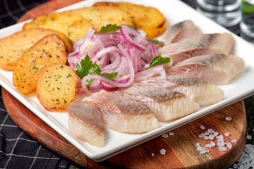 White plate of pieces of pickled herring, chopped chives with fried potato, onion, tomato and cold vodka. Russian traditional cuisine. Close up.