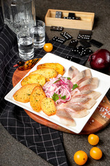 White plate of pieces of pickled herring, chopped chives with fried potato, onion, tomato and cold vodka. Russian traditional cuisine. Close up.