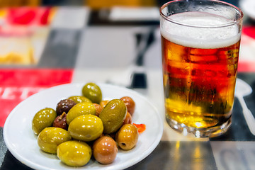 Closeup view of Spanish tapa of fresynolives and chilled glass of beer on colorful tablecloth.