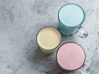 Trendy drinks: Blue, yellow and pink latte. Top view of hot butterfly pea or blue spirulina latte, yellow or gold turmeric latte and pink beetroot latte on gray cement background. Copy space for text