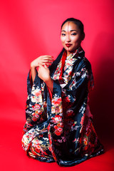 young pretty geisha on red background posing in kimono, oriental concept