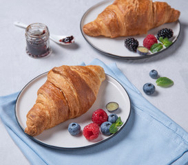 two fresh  croissant on a white plate  with jam, blueberries and raspberries on a gray background